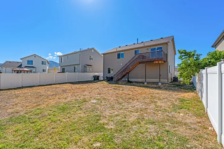 Expansive backyard featuring a privacy fence, wood deck, and exterior stairs