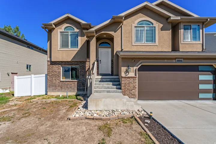 Stucco exterior with brick accents, arched entry, concrete steps, and a contemporary garage door with frosted glass panels
