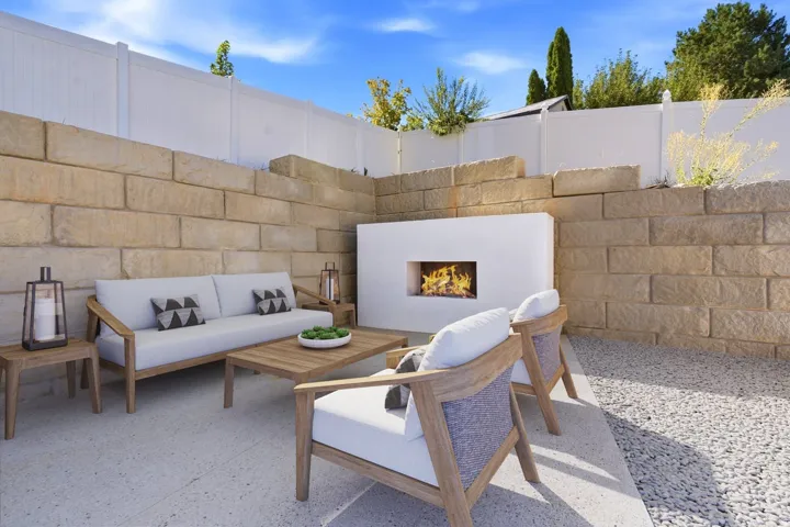 Outdoor living area featuring a built-in fireplace, stone retaining walls, privacy fencing, and a concrete patio with a decorative gravel border