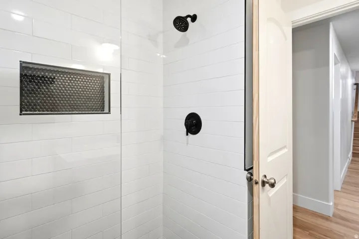 Glass-enclosed shower with white subway tile, matte black fixtures, and a recessed niche featuring mosaic tile