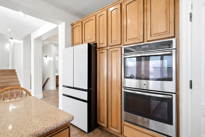 Built-in stainless steel double ovens, wood cabinetry, refrigerator, and stone-finish countertop