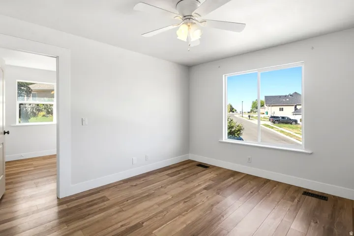 Spacious room featuring wood-finish flooring, a ceiling fan with integrated lighting, and a large window with white trim