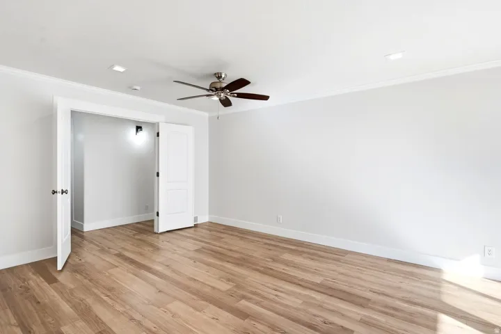 Wood-finish flooring, white paneled doors, ceiling fan, recessed lighting, and crown molding