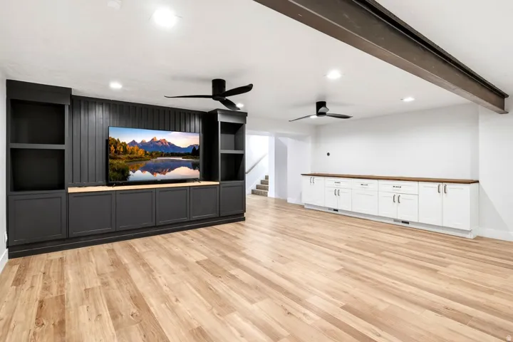 Built-in media center with shelving, recessed lighting, wood-finish flooring, two ceiling fans, and extensive built-in white cabinetry with wood countertops