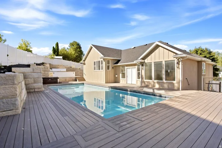 Expansive outdoor living area featuring a swimming pool, composite decking, and tiered landscaping with stone retaining walls