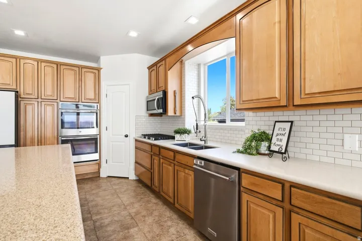 Warm wood cabinetry, stainless steel appliances, solid surface countertops, white subway tile backsplash, and tile flooring