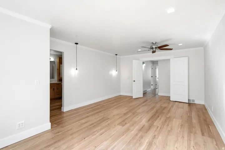 Wood-finish flooring, white crown molding, recessed lighting, and a ceiling fan with integrated lighting