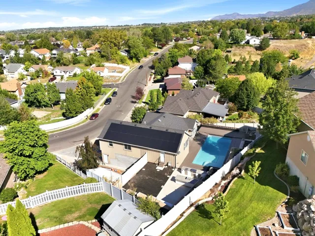 Expansive swimming pool with surrounding deck, solar panels on the roof, mature landscaping, and white fencing