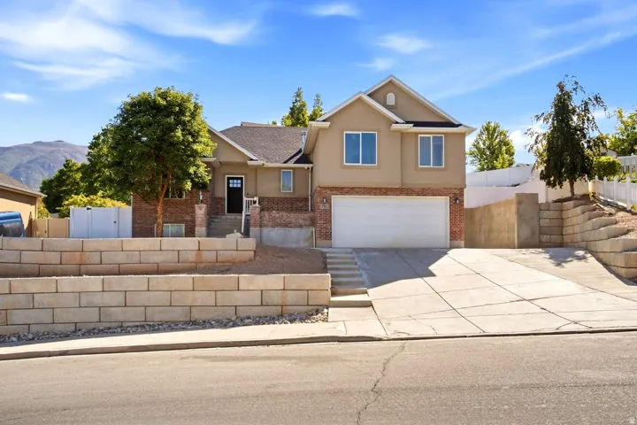 Two-story residence featuring a brick and stucco exterior, an attached two-car garage, concrete driveway, and tiered retaining walls