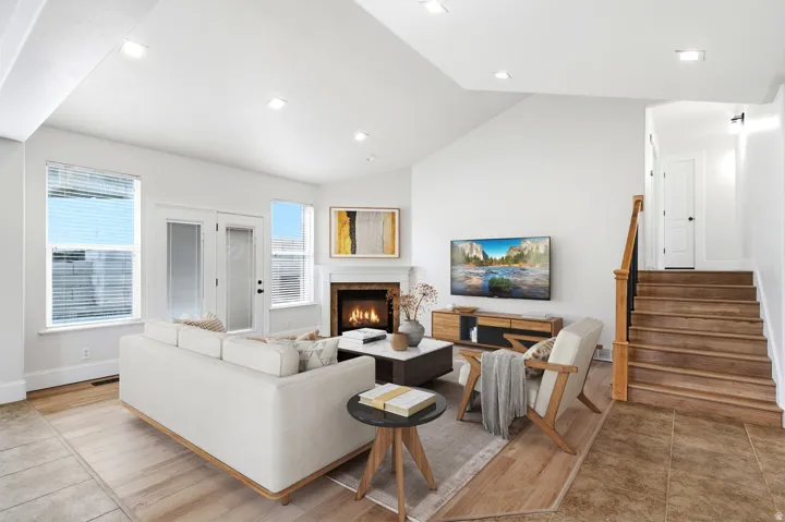 Vaulted ceiling with recessed lighting, wood-finish flooring, corner fireplace with mantel, double-paned glass door, and wood staircase with railing