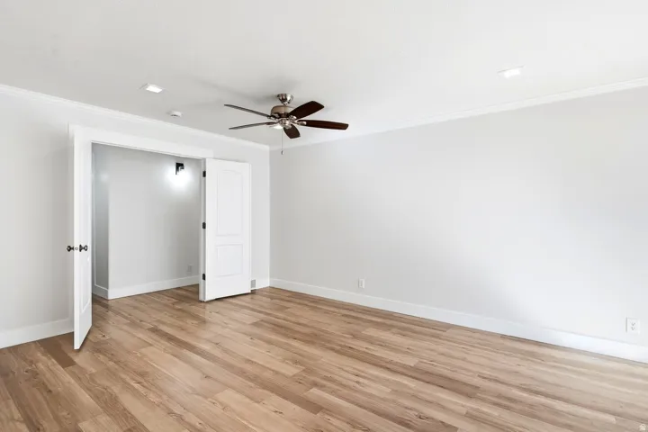 Wood-finish flooring, ceiling fan, recessed lighting, white interior doors, and crown molding