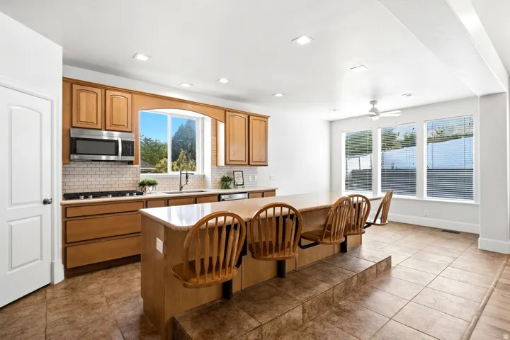 Kitchen with wood cabinetry, stainless steel appliances, subway tile backsplash, and a large island with tiered seating