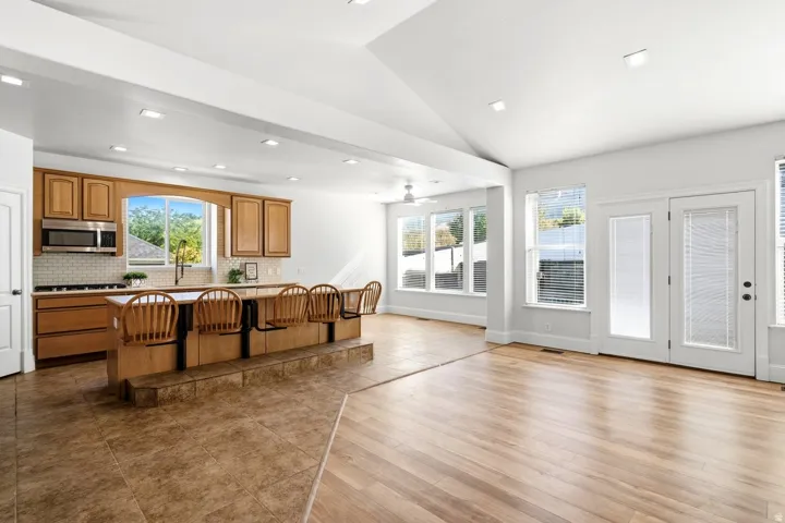 Vaulted ceilings with recessed lighting, wood-finish flooring, kitchen with light wood cabinetry, stainless steel microwave, and French doors