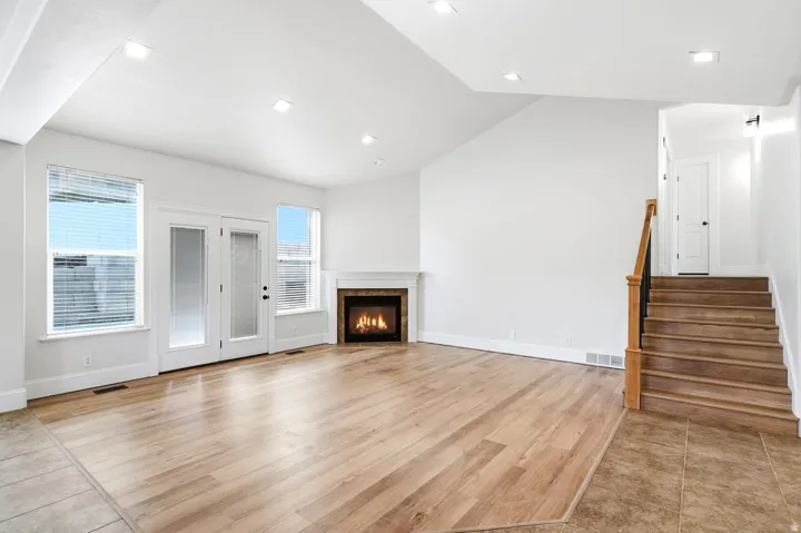 Spacious living area featuring wood-finish flooring, a corner fireplace with a stone surround, recessed lighting, and a white wood mantel