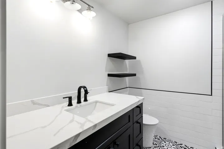 White subway tile walls, patterned floor tile, white vanity countertop, black vanity cabinetry, and matte black fixtures