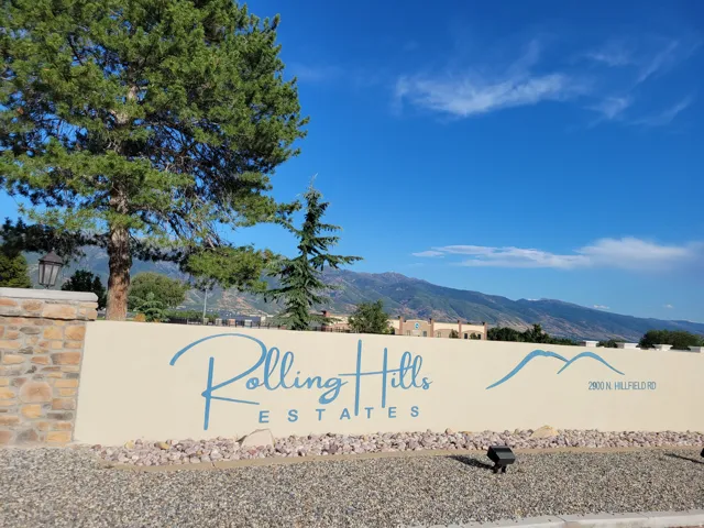 Rolling Hills Estates community entrance featuring a stone-clad pillar with an integrated lantern, a prominent community sign, and a mountainous backdrop