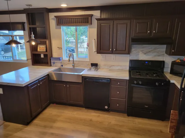 Kitchen featuring dark wood-finish cabinetry, light-toned countertops, stainless steel farmhouse sink, and black appliances