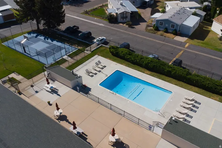 Outdoor swimming pool with surrounding concrete decking, fenced perimeter, and adjacent tennis court