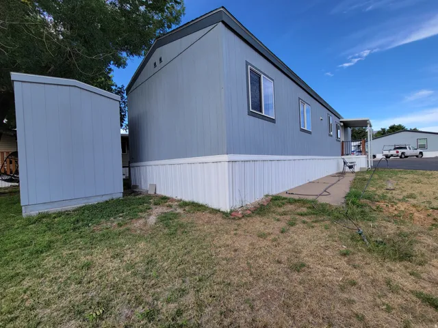 Exterior featuring gray siding and white trim, multiple windows with white frames, a covered entry, and a detached storage shed