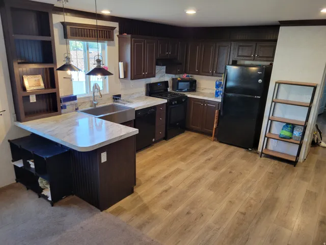 Kitchen featuring wood-finish flooring, dark wood cabinetry, light-toned countertops, a stainless steel farmhouse sink, and a built-in shelving unit