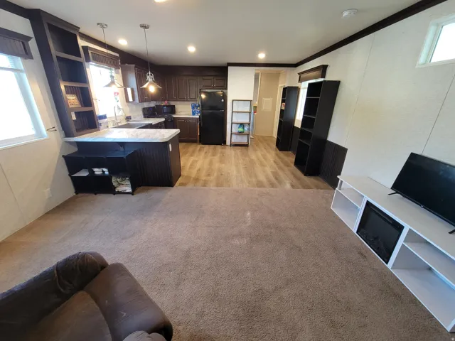 Open-concept living space featuring wood-finish flooring, a kitchen with dark cabinetry, and a breakfast bar with an integrated shelving unit