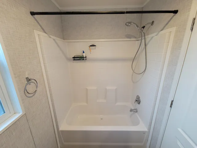 Tub and shower combination with white tile-finish surround and textured wall covering
