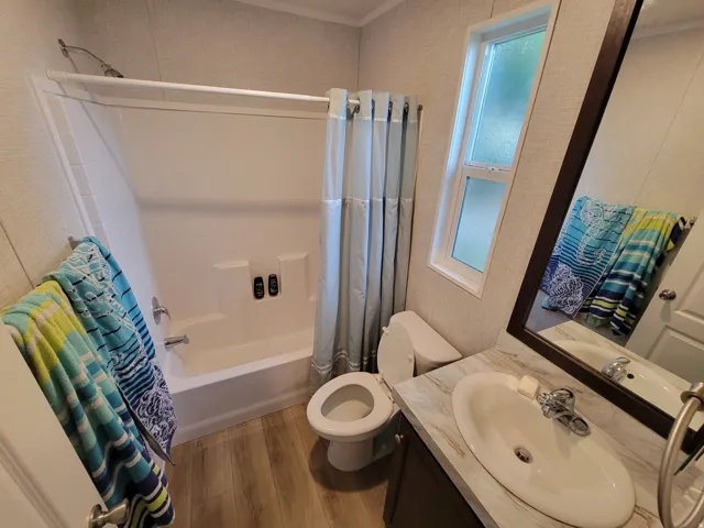 Full bathroom featuring a white tub/shower combination, a single vanity with an integrated sink, a large framed mirror, and wood-finish flooring