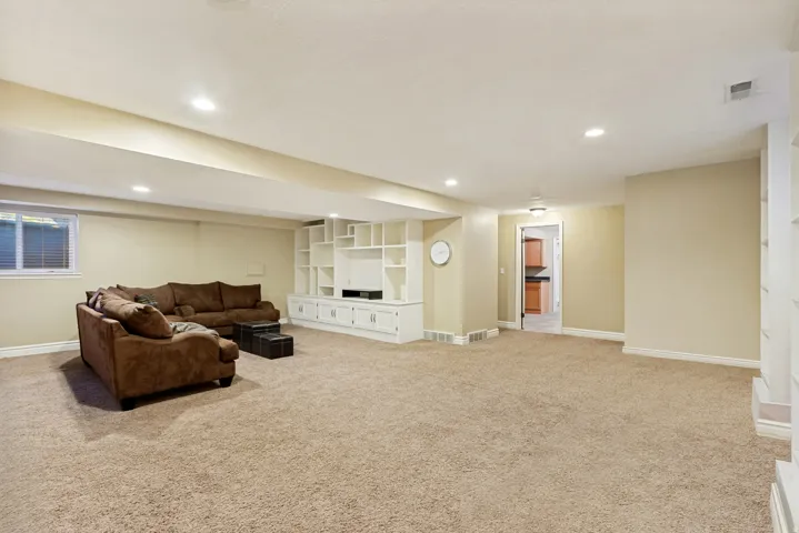 Spacious carpeted living area featuring recessed lighting, a built-in media center with shelving and lower cabinetry, and a window with blinds