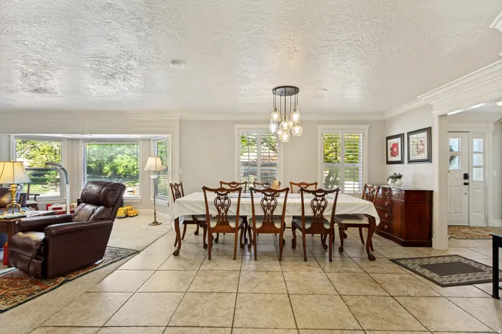 Tile flooring throughout, recessed bay window, contemporary multi-bulb chandelier, white window shutters, and a paneled entry door