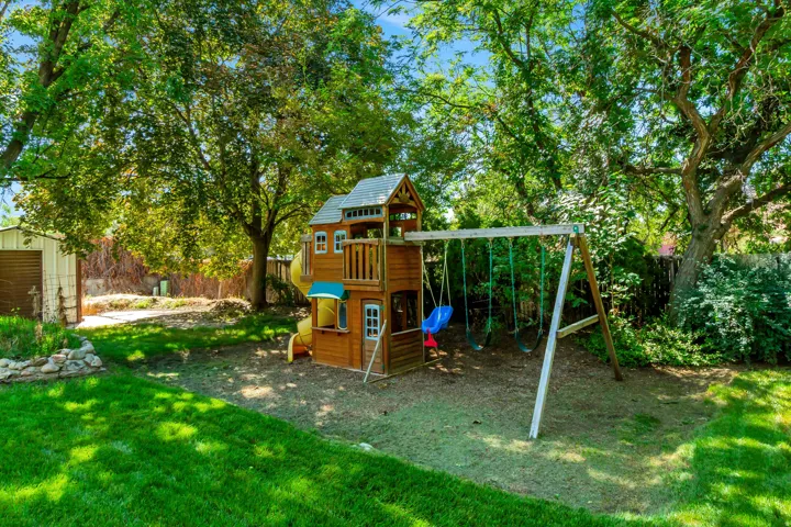 Expansive backyard featuring a wood-finish playset, swing set, and mature trees