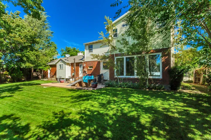 Expansive rear yard featuring a large patio, lush lawn, mature trees, and a two-story exterior with brick and siding