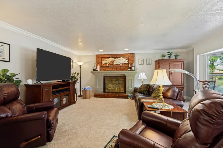Brick fireplace with a painted mantel, carpeted flooring, and crown molding