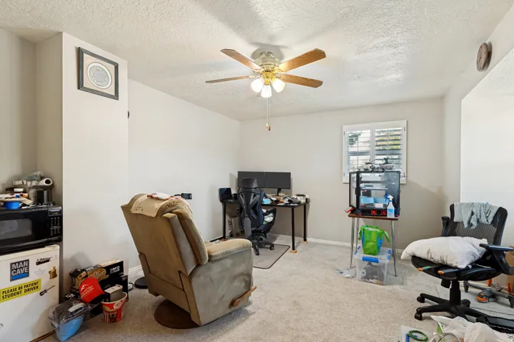 Carpeted room featuring a ceiling fan with light fixture and a window with white shutters