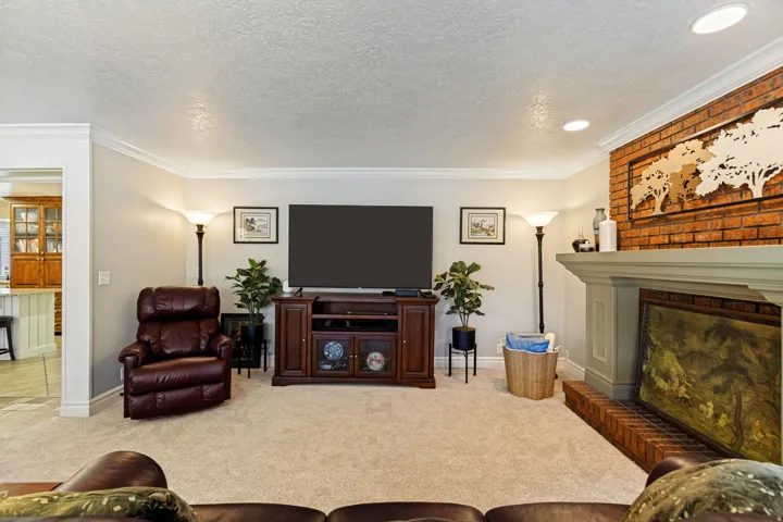 Carpeted living area with a built-in brick fireplace, painted mantel, and crown molding