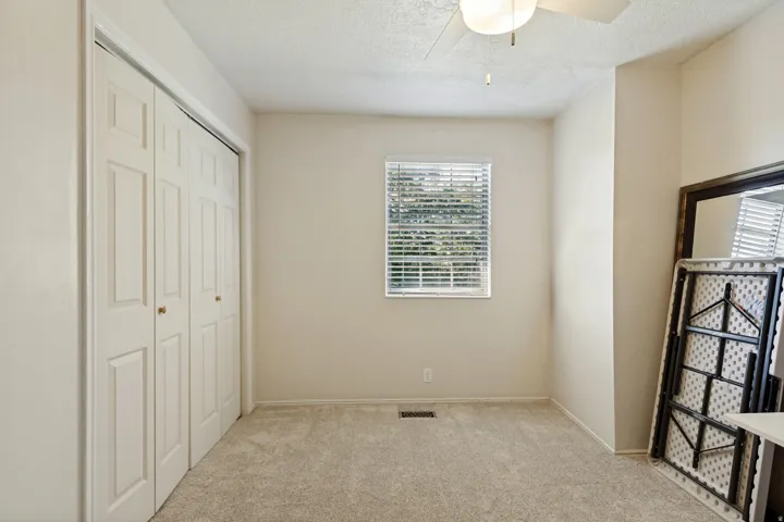 Neutral carpet flooring, bi-fold closet doors, window with blinds, and ceiling fan