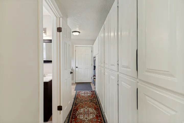 Hallway next to kitchen with extensive built-in white cabinetry, recessed overhead lighting, and a paneled interior door. Bathroom and laundry room
