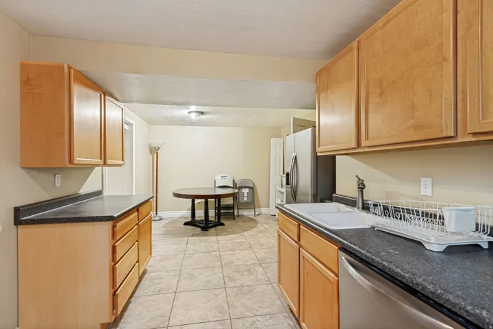 Kitchen featuring wood cabinetry, dark countertops, a stainless steel dishwasher, and tile flooring