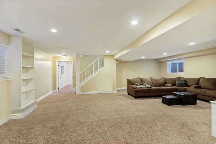 Recessed lighting, built-in shelving, carpet flooring, staircase with white balusters, and a window with blinds