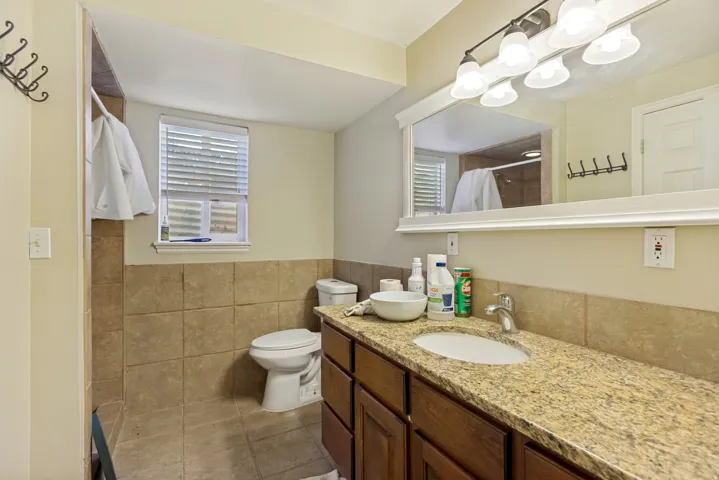 Tile flooring, tile wainscoting, wood-finish vanity, stone-finish countertop, and an integrated sink with a chrome faucet