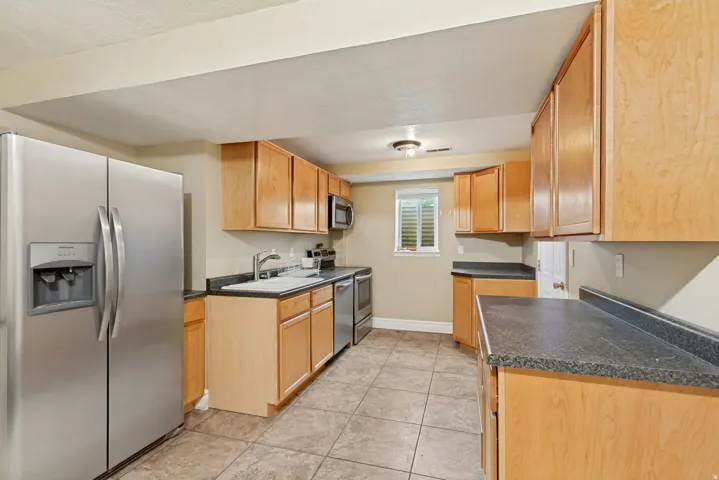 Kitchen featuring wood-finish cabinetry, stainless steel appliances, dark countertops, and tiled flooring
