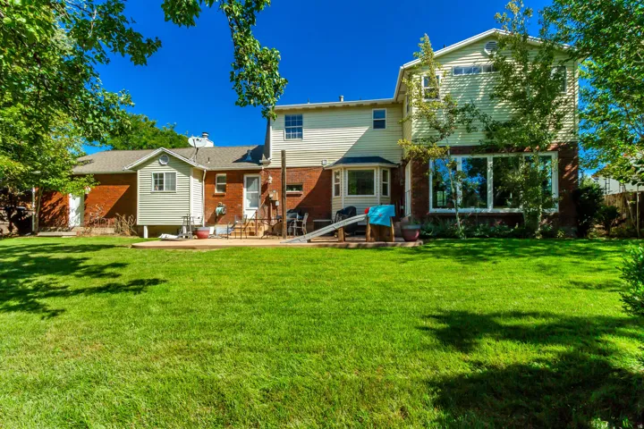 Expansive backyard with a large grass lawn, brick exterior, and a ground-level patio