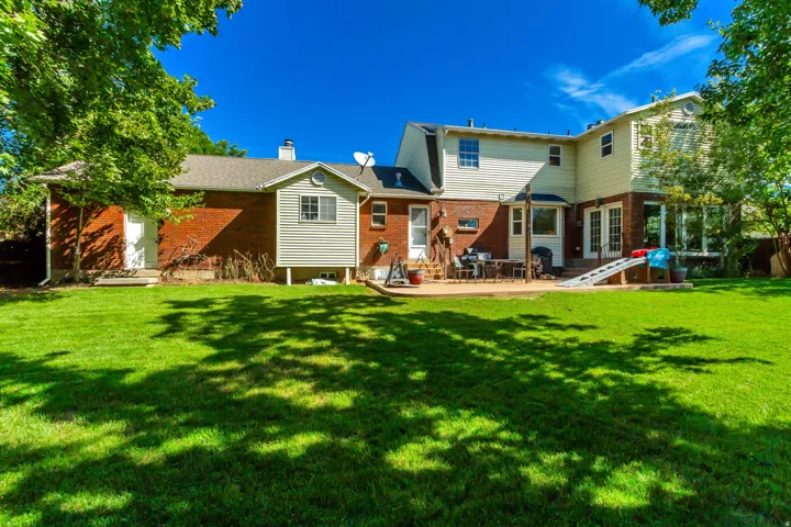 Expansive green lawn, multi-level home exterior, brick and siding facade, patio area, mature trees