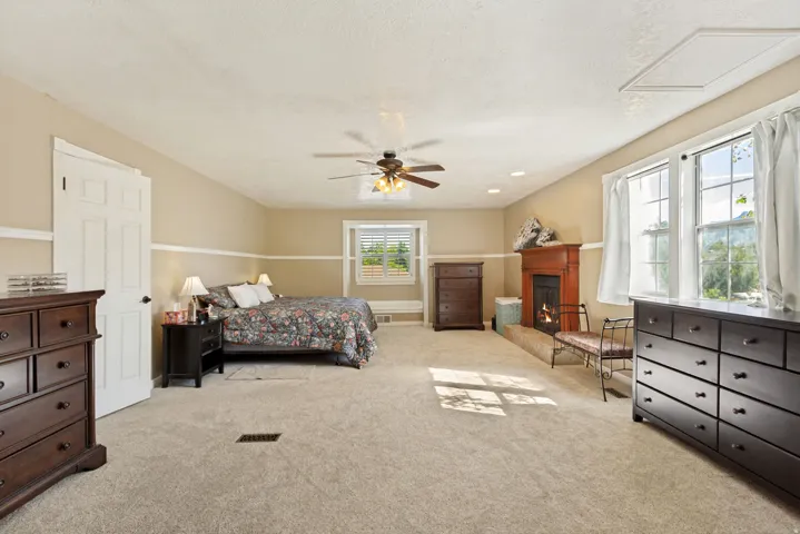 Spacious room featuring neutral carpeting, a wood-surround fireplace, a ceiling fan, and multiple windows providing natural illumination