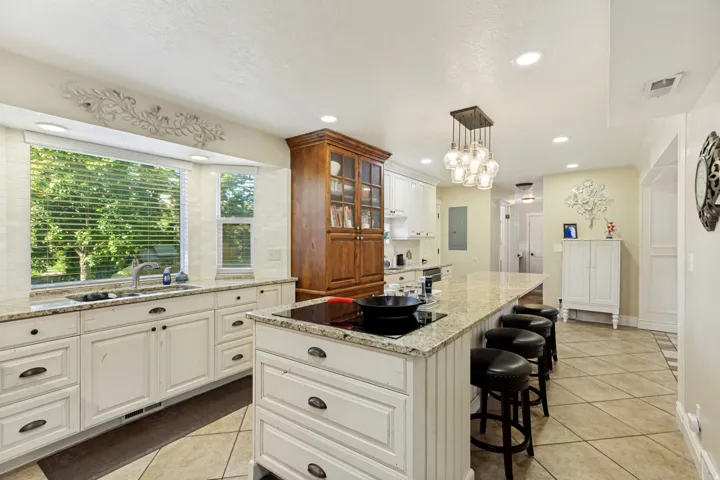 Kitchen featuring a large bay window, white cabinetry with dark hardware, a built-in cooktop island with seating, a wood-finish display cabinet, and recessed ceiling lighting