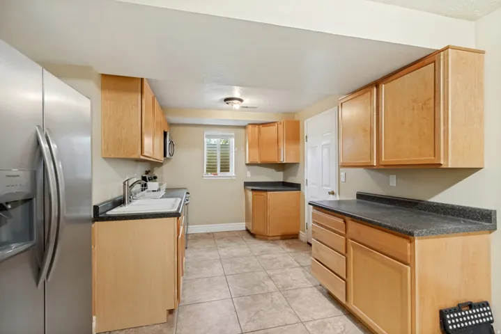Kitchen featuring wood-finish cabinetry, dark countertops, a stainless steel refrigerator, and tiled flooring