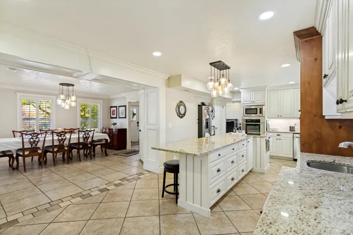 Kitchen featuring granite countertops, white cabinetry, built-in appliances, a central island with seating, and tile flooring with decorative inlay