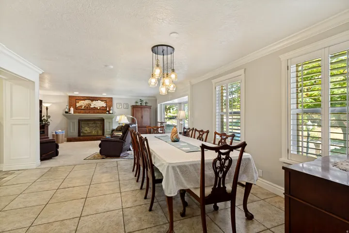 Tile flooring, crown molding, plantation shutters, brick fireplace with mantel, and a multi-bulb chandelier