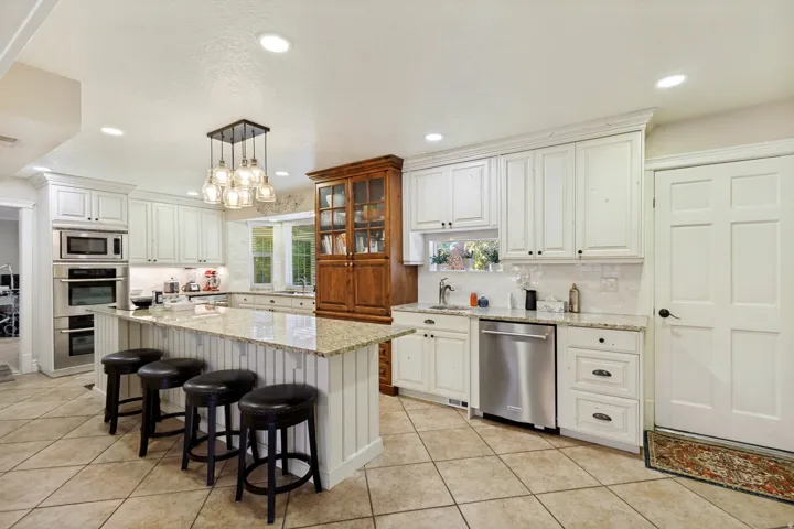 Kitchen featuring white cabinetry, built-in stainless steel appliances, a center island with countertop seating, and a decorative pendant light fixture