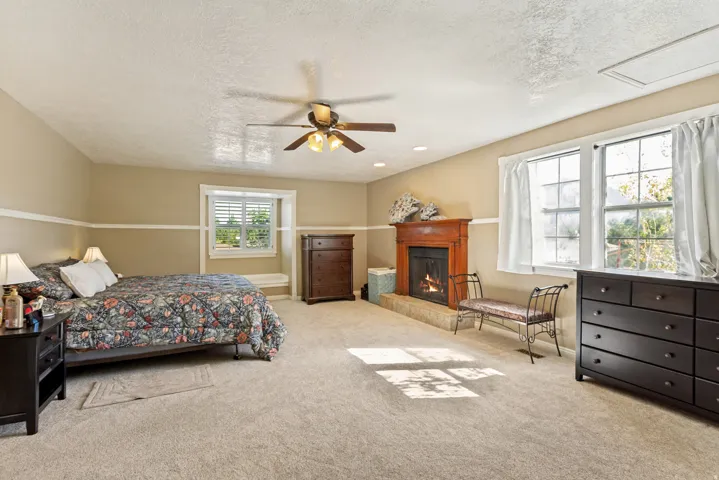 Carpeted room featuring a ceiling fan, fireplace with wood mantel, and multiple windows