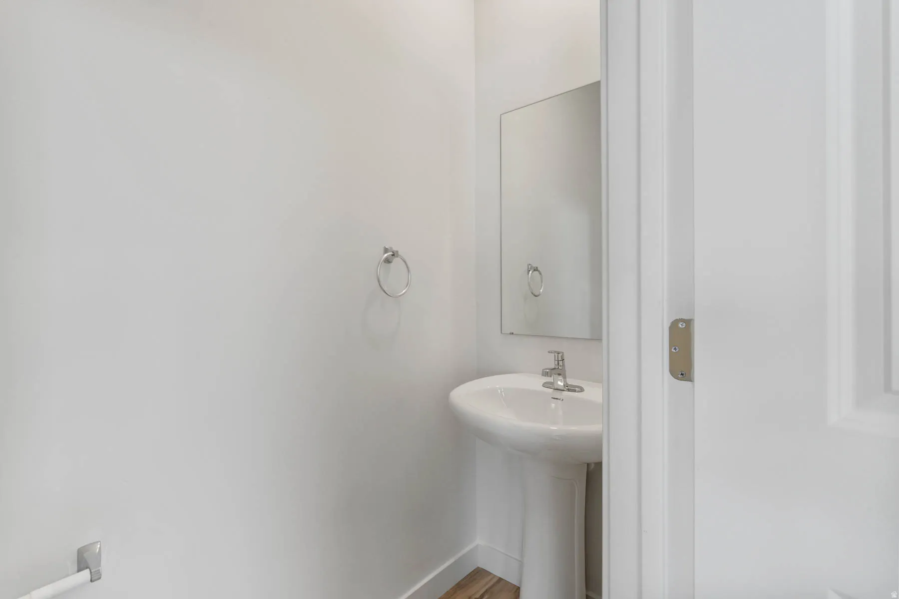 Pedestal sink with chrome faucet, wall-mounted mirror, and wood-finish flooring